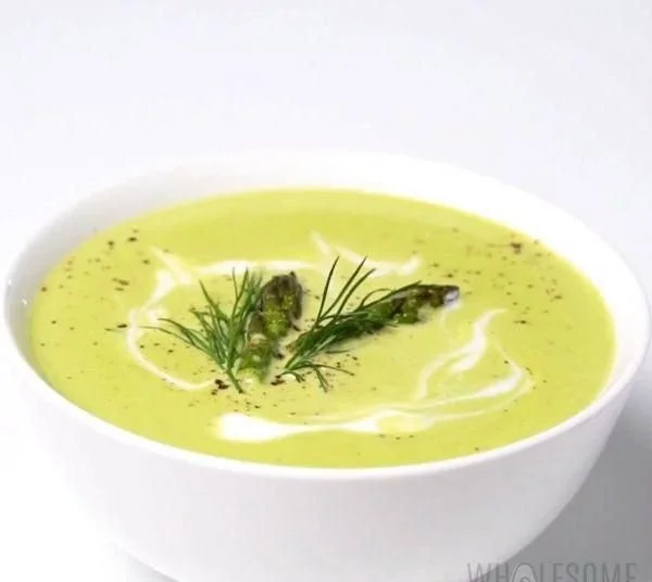 Bowl of creamy asparagus soup garnished with fresh herbs