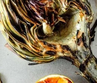 Delicious grilled artichoke on a wooden platter with lemon.