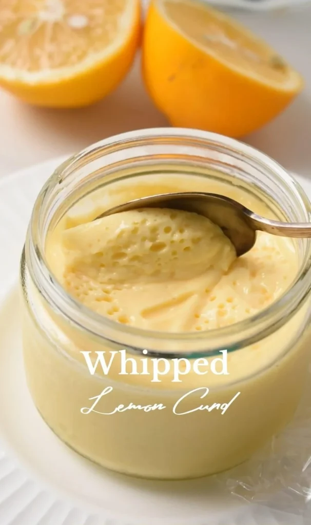 Homemade lemon curd in a jar with fresh lemons and a whisk nearby.