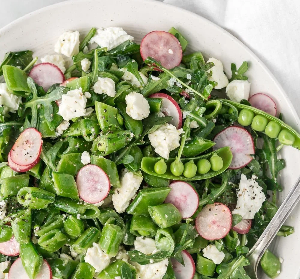 Colorful sugar snap pea salad with radishes, feta, and arugula on a plate