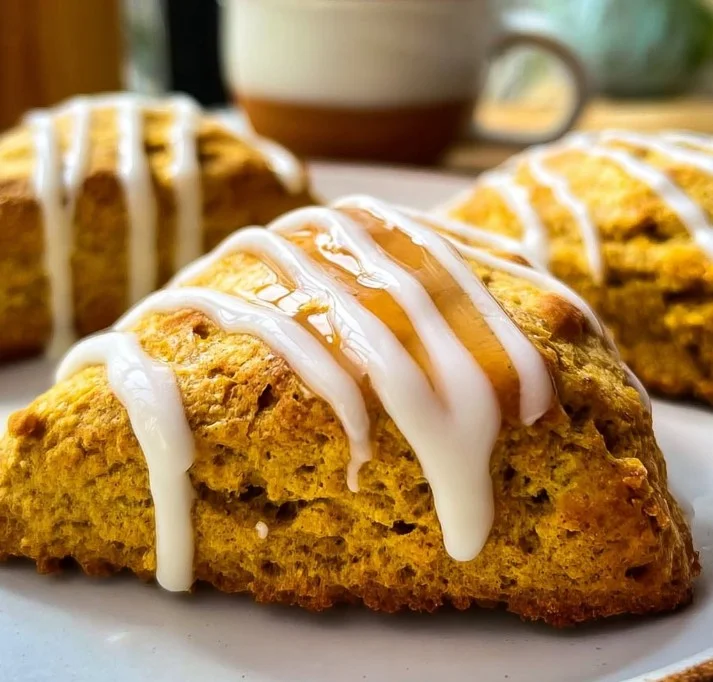 Homemade pumpkin scones with warm spices and glaze on a wooden board.